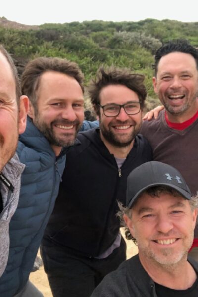 a group of men smiling at the camera on a beach, arm in arm